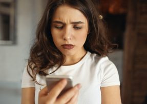 Mladá žena nevěřícně kouká na mobil