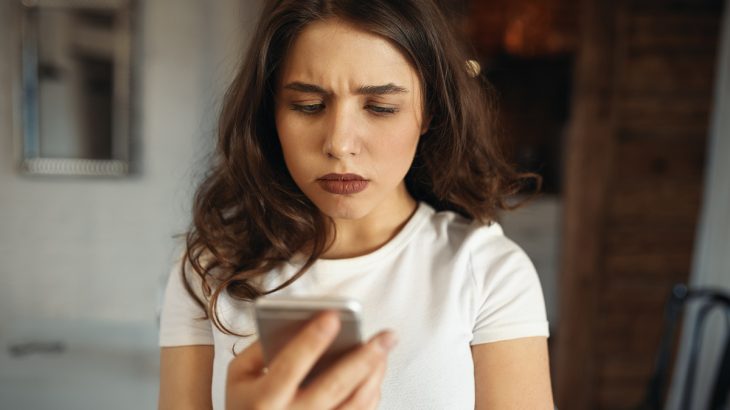 Mladá žena nevěřícně kouká na mobil