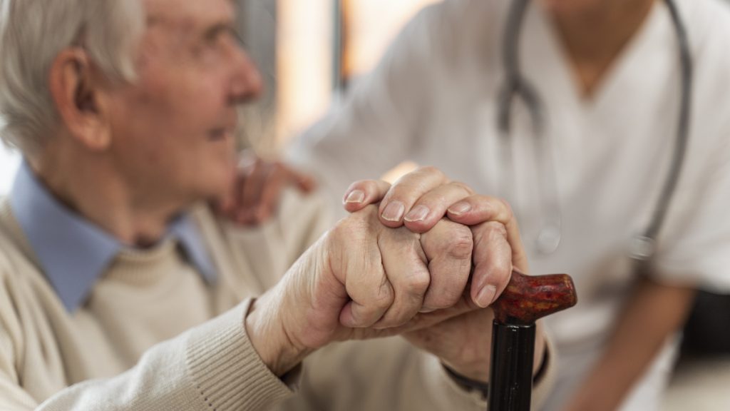 Starý muž se opírá o hůl a mluví s lékařem