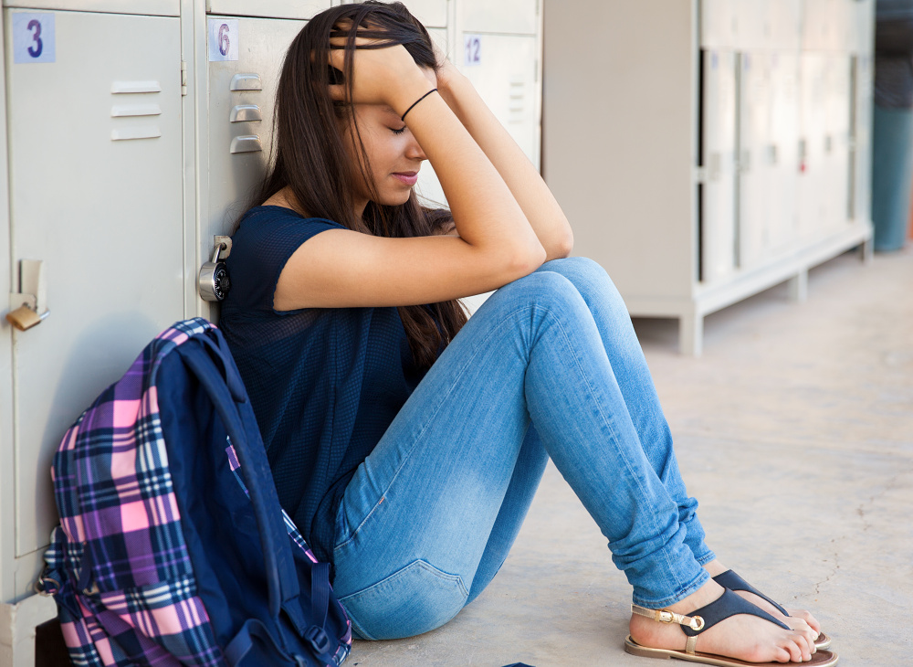 Smutná studentka sedí u školních skříněk
