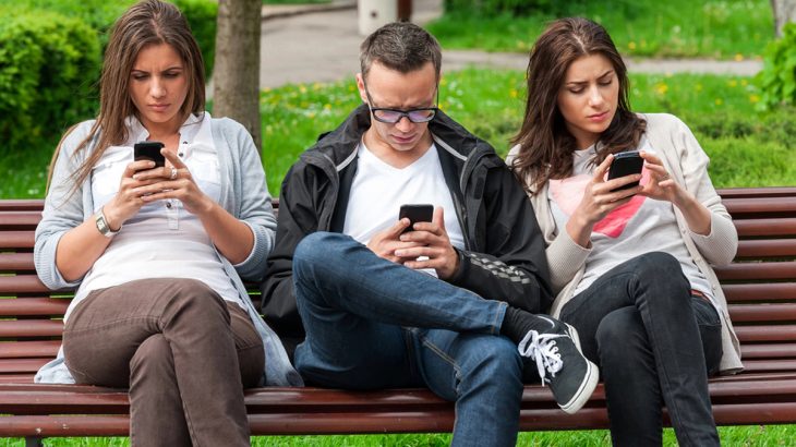 Lidé v parku na lavičce koukají na mobily