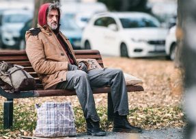 Bezdomovec na lavičce v parku
