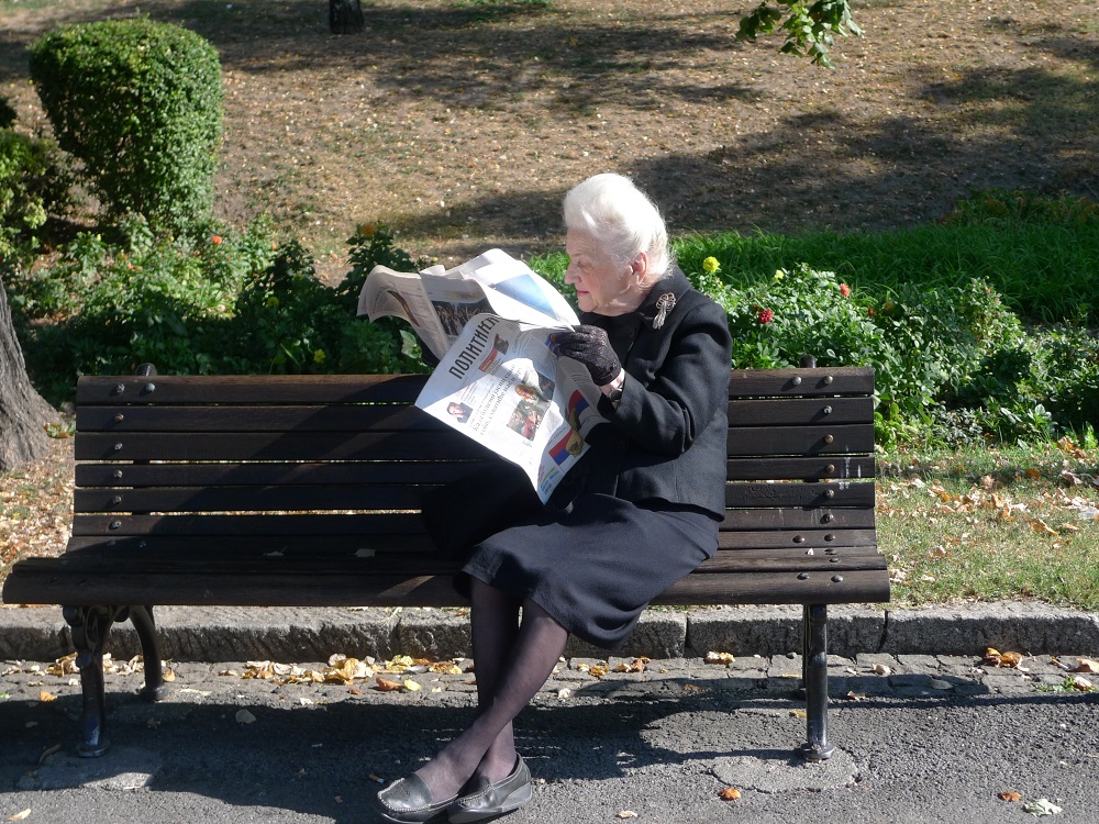 Žena čte noviny na lavičce